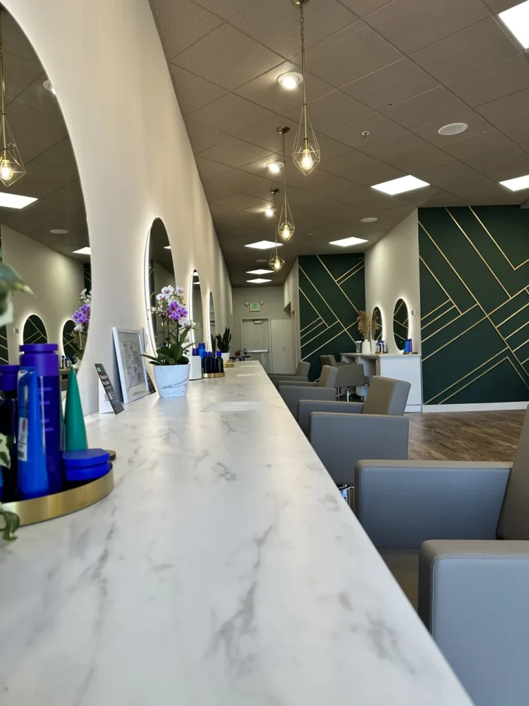 Styling floor at Vamp Salon Extension Studio, a hair salon in Brentwood, CA, with a marble color bar, arched lit mirrors, and gold pendant lights