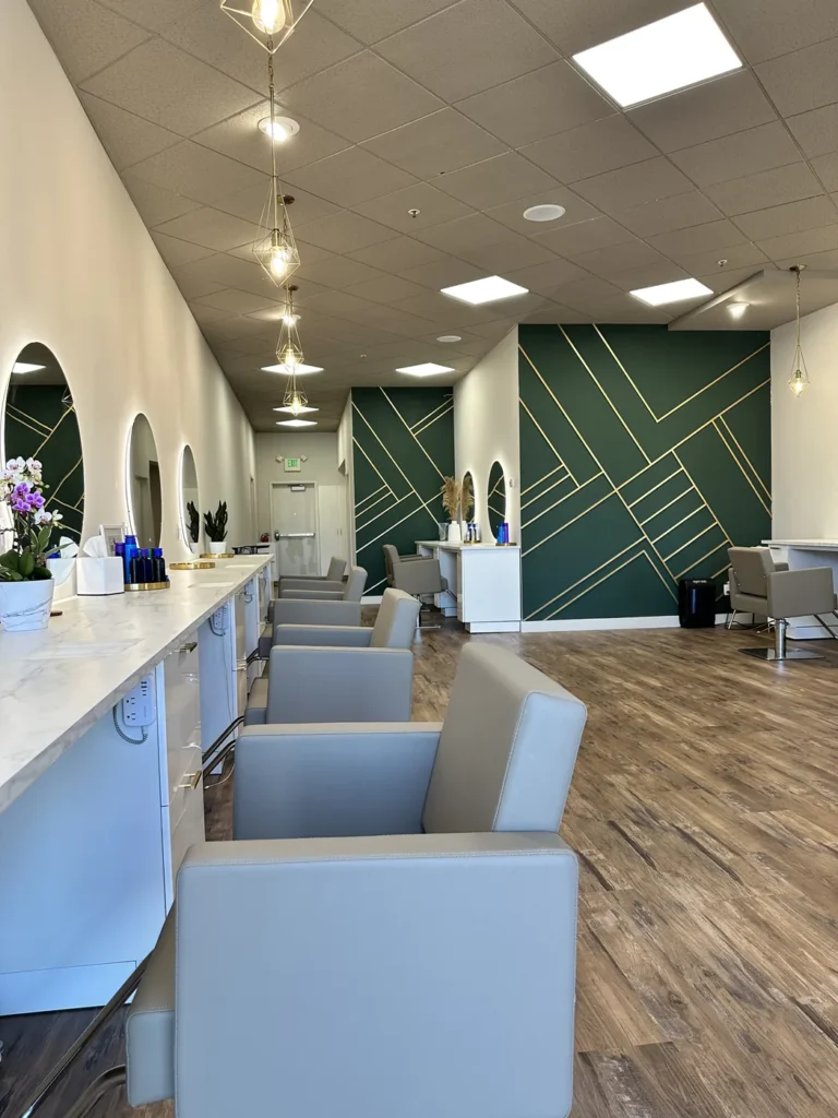 Styling stations at Vamp Salon Extension Studio, a hair salon in Brentwood, CA, with arched lit mirrors and a green and gold geometric feature wall