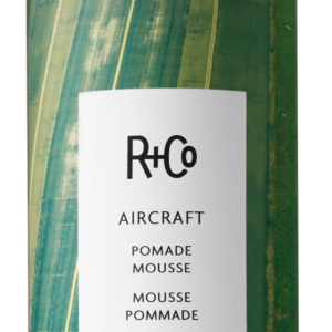 Squeeze bottle labeled R+Co Aircraft Pomade Mousse with a green airplane-themed label.
